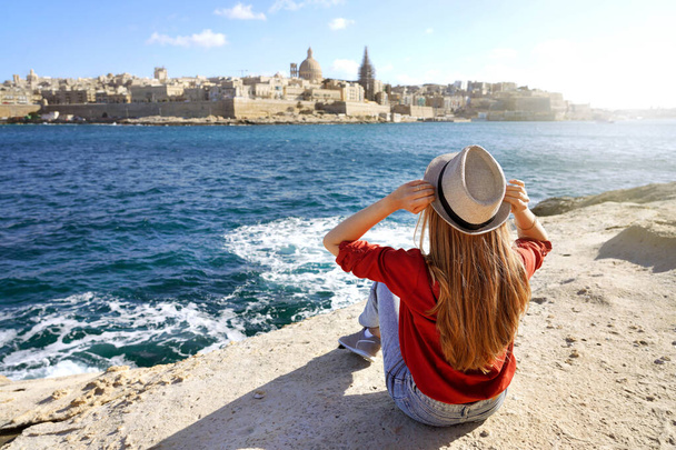 Νεαρή ταξιδιώτισσα κρατά καπέλο κοιτάζοντας Valletta παλιά πόλη ταξιδιωτικό προορισμό στη Μάλτα - Φωτογραφία, εικόνα
