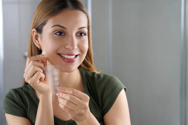 Menina sorridente aplicando tratamento de acne patch anti-pickel em uma espinha no banheiro em casa - Foto, Imagem