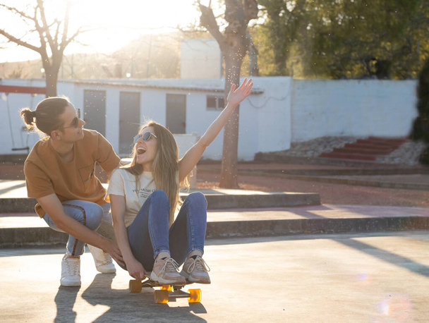 Heterosexual young couple having a good time while using a longboard in the afternoon light - Zdjęcie, obraz
