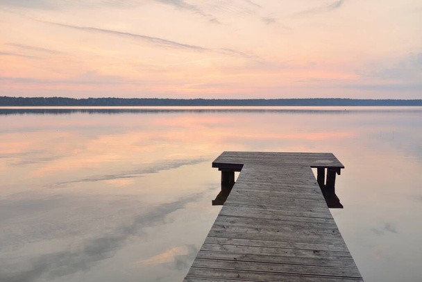 Forest lake at sunset. Wooden pier. Soft sunlight, glowing clouds, symmetry reflections in a crystal clear water. Idyllic landscape. Panoramic view. Nature, ecology, ecotourism. Peace and joy concepts - Foto, Imagen