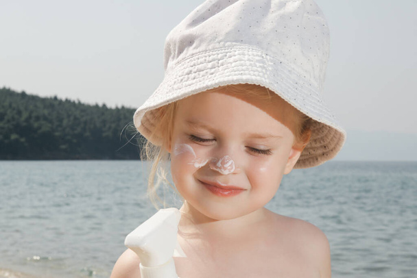Küçük tatlı kız plajda güneş kremi sürüyordu. Yaz tatilinde bebeği güneşten korumak için güneş kremi. Yolculuk sırasında çocukların cilt bakımı. - Fotoğraf, Görsel