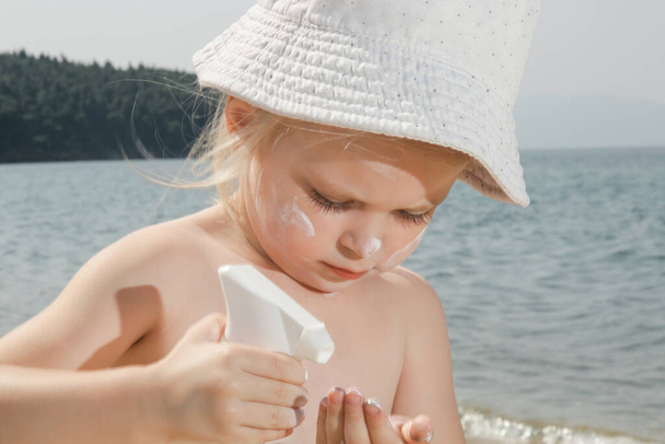 Roztomilé malé batole dívka použití krém na ochranu proti slunečnímu záření na pláži. Krém proti slunci na ochranu dítěte před sluncem během letních prázdnin. Děti péče o pleť během cesty. - Fotografie, Obrázek