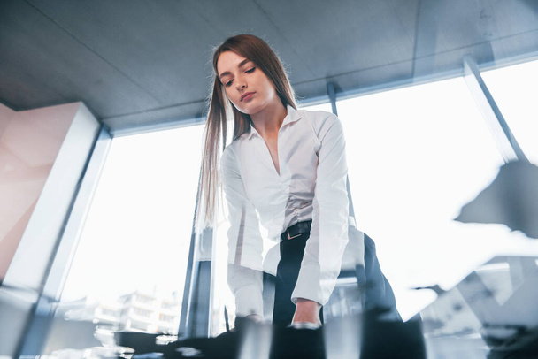 View from below. Young woman in white formal clothes is indoors in the modern office. - Foto, immagini