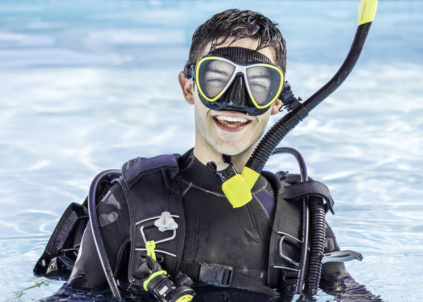 Onnellinen nuori mies sukellusvarusteet päällä uima-altaassa hymyillen kameralle. - Valokuva, kuva