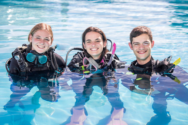 A group of happy scuba divers standing in a pool with their gear on smiling at the camera - Foto, imagen