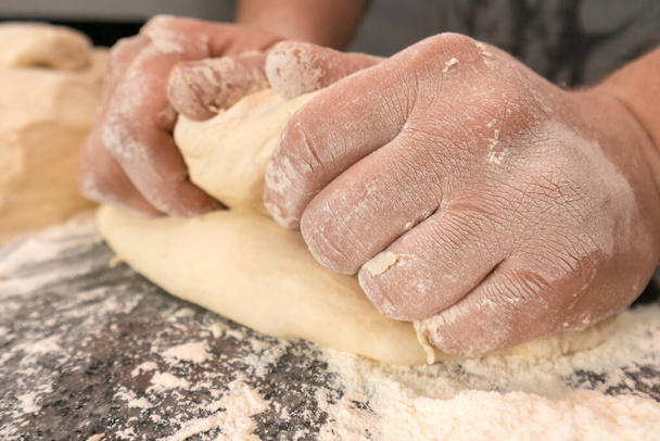 Close-up of men's hands kneading elastic yeast dough on a table sprinkled with flour - Fotó, kép