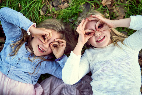 Všechno je zábavné, když jsi mladý. Portrét dvou malých sester ležících venku na trávě. - Fotografie, Obrázek
