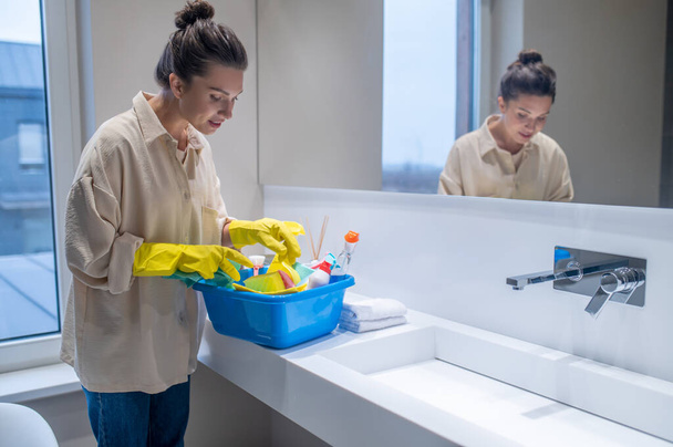 A young woman with a box with detergents in the bathroom - Foto, imagen