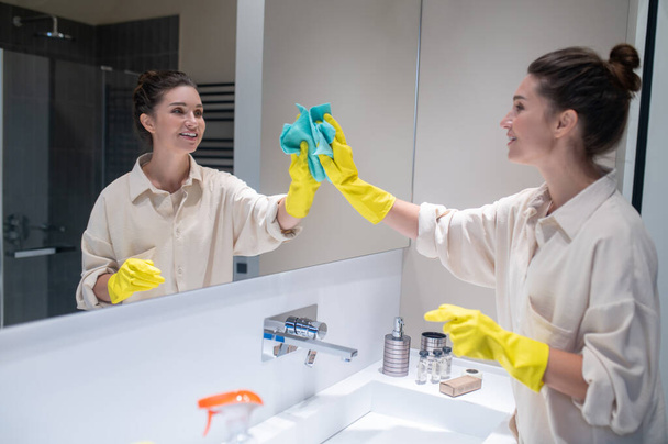 Cute young woman cleaning mirror in the bathroom - Φωτογραφία, εικόνα