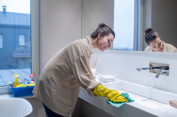 A young woman in yellow gloves cleaning the surfaces in the bathroom - Fotografie, Obrázek