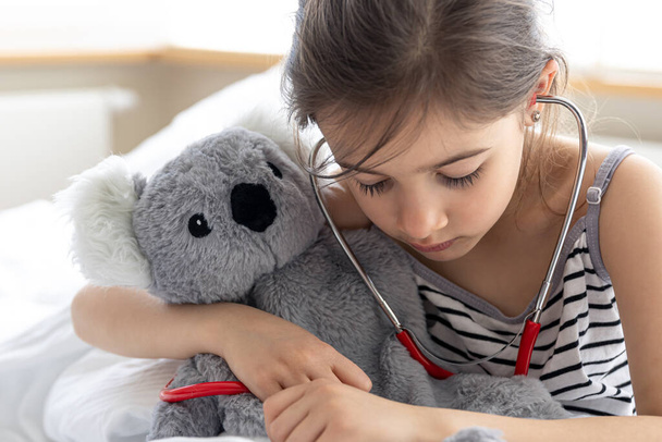 A little girl plays doctor with her favorite soft toy. - Fotó, kép