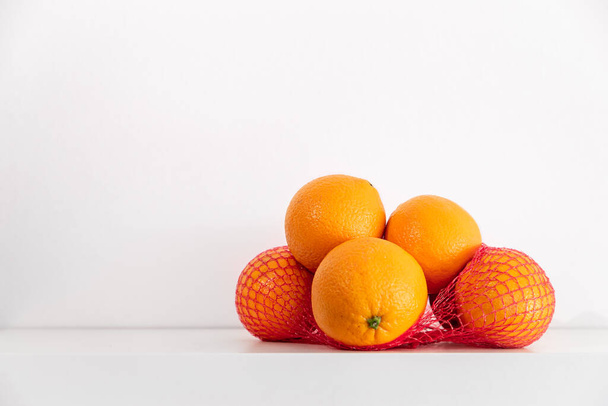 Свежие апельсины в сетке на полке на белом фоне. - Фото, изображение