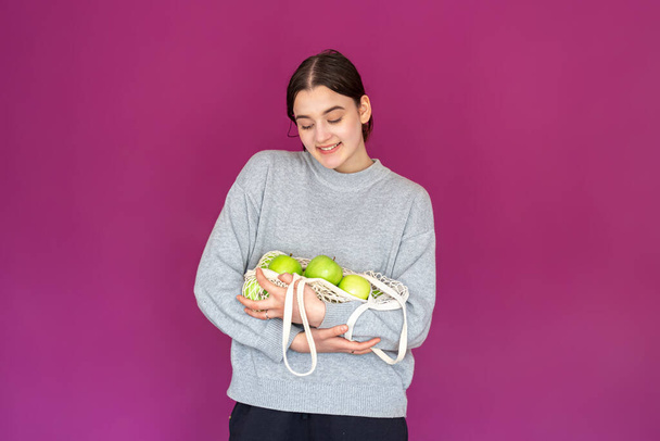 A young woman with a string bag with apples on a pink background. - Photo, Image
