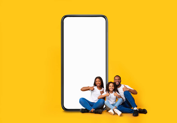 Черная семья показывает пустой экран смартфона и большие пальцы вверх - Фото, изображение