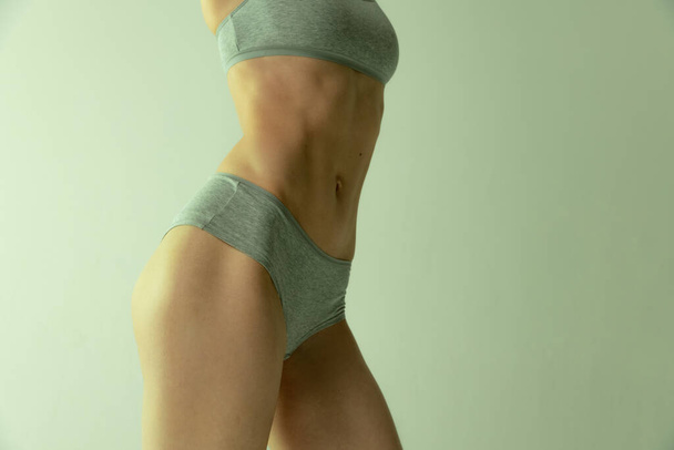 Cropped image of slim muscular female body in cotton underwear isolated over grey studio background. Fit body - Foto, Imagem