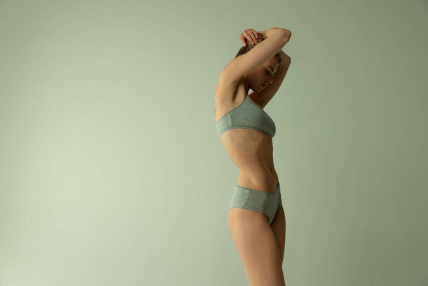Porträt einer schlanken, muskulösen jungen Frau, die in Unterwäsche isoliert vor grauem Studiohintergrund posiert. Perfekte Körperform - Foto, Bild