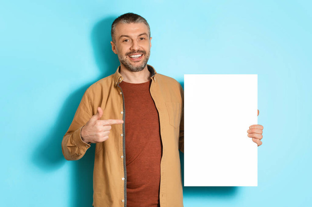 Middle Aged Man Showing Empty White Paper On Blue Background - Fotoğraf, Görsel
