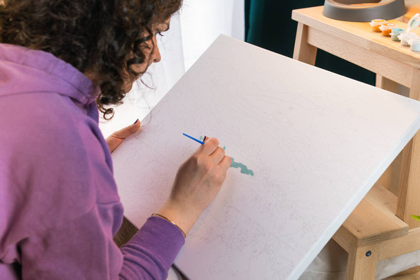 Η ενήλικη γυναίκα ζωγραφίζει με αριθμούς σε εσωτερικούς χώρους. Έννοιες της δραστηριότητας αναψυχής, χόμπι και να χαλαρώσετε - Φωτογραφία, εικόνα