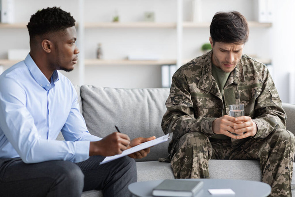 Üzgün asker psikologla terapi seansı yapıyor, klinik içişleri. - Fotoğraf, Görsel
