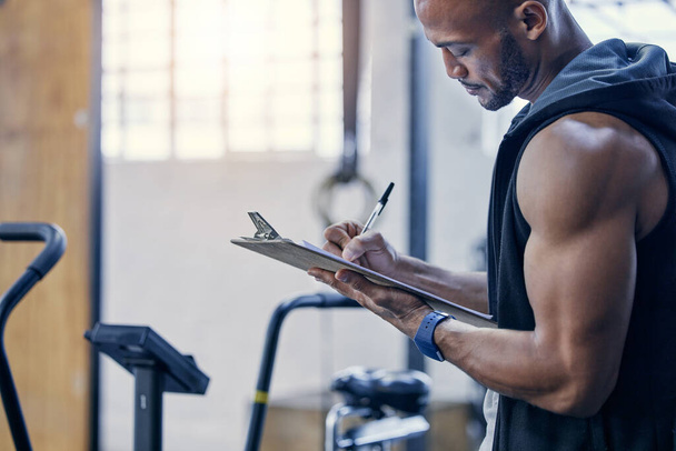 Organising and stocking supplies for all gym patrons. Shot of a muscular young man writing notes on a clipboard while working in a gym. - Photo, Image