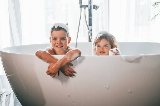 Deux enfants s'amusent et se lavent dans le bain à la maison. Poser pour un appareil photo. - Photo, image