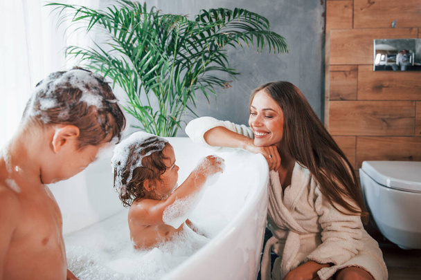 Having fun. Young mother helps her son and daughter. Two kids washing in the bath. - Foto, immagini