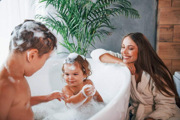 Having fun. Young mother helps her son and daughter. Two kids washing in the bath. - Foto, Bild