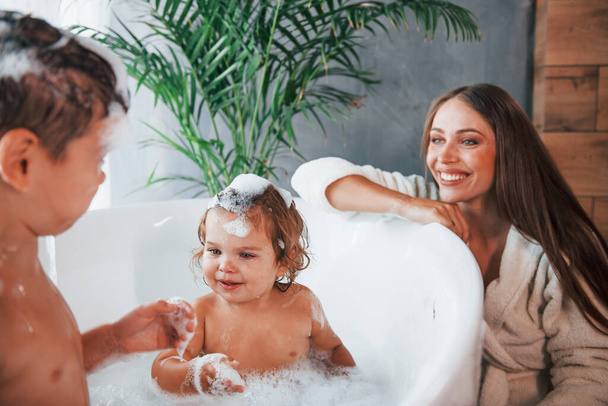 Having fun. Young mother helps her son and daughter. Two kids washing in the bath. - Valokuva, kuva