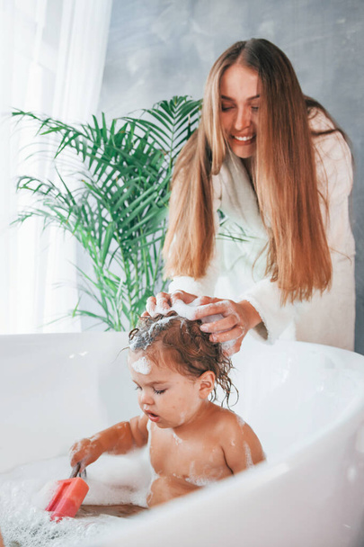Young mother helps her daughter to wash in the bath. - Valokuva, kuva