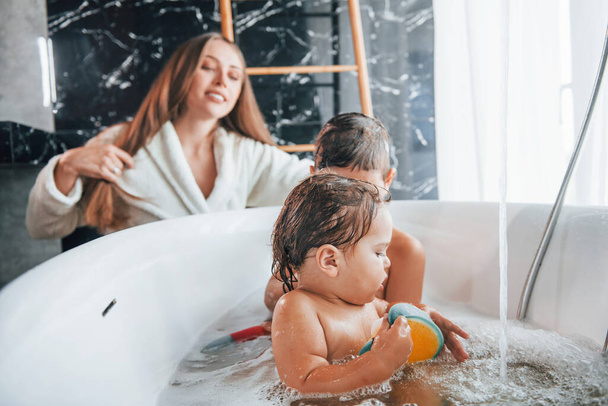 Having fun. Young mother helps her son and daughter. Two kids washing in the bath. - Фото, зображення