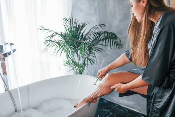 Beautiful young woman have free time at home in the bath. Shaves legs. - Fotografie, Obrázek