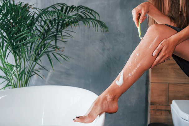 Beautiful young woman have free time at home in the bath. Shaves legs. - Foto, afbeelding
