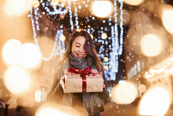 With gift box. Cute and happy asian young woman outdoors in the city celebrates New year. - Foto, Imagen