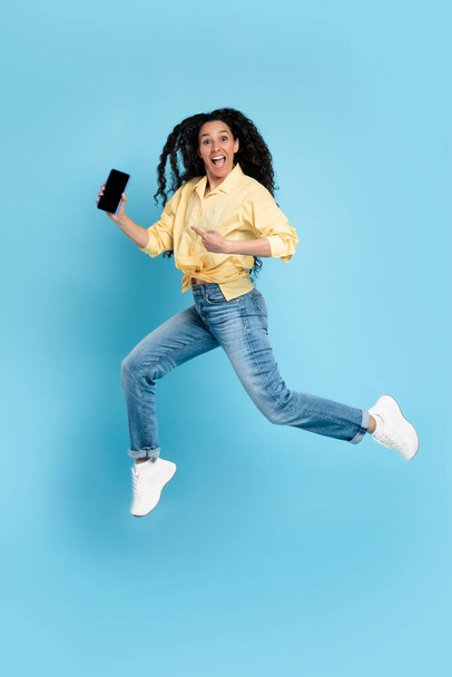 Cheerful lady jumping and pointing at empty smart phone screen - Valokuva, kuva