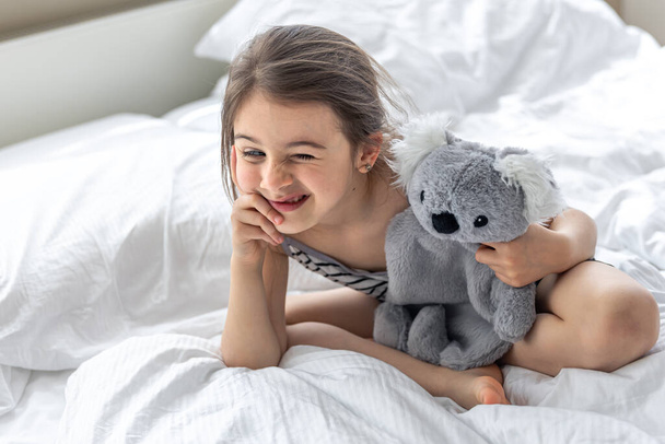 Glückliches kleines Mädchen mit Stofftier-Koala im Bett. - Foto, Bild