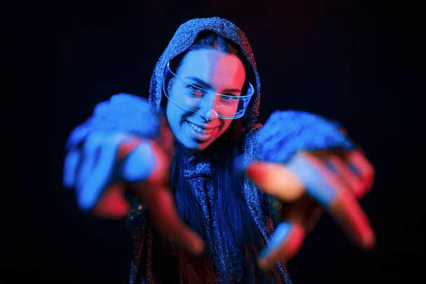 Does gestures by hands. Portrait of young girl that is in eyeglasses in blue neon lighting. - Fotografie, Obrázek