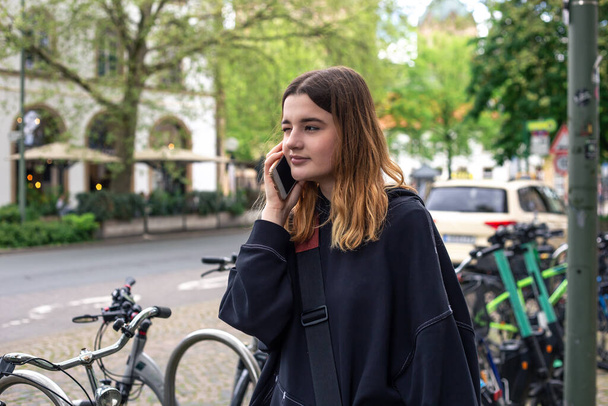 Μια νεαρή γυναίκα μιλάει στο τηλέφωνο σε ένα πάρκινγκ ποδηλάτων στην πόλη.. - Φωτογραφία, εικόνα