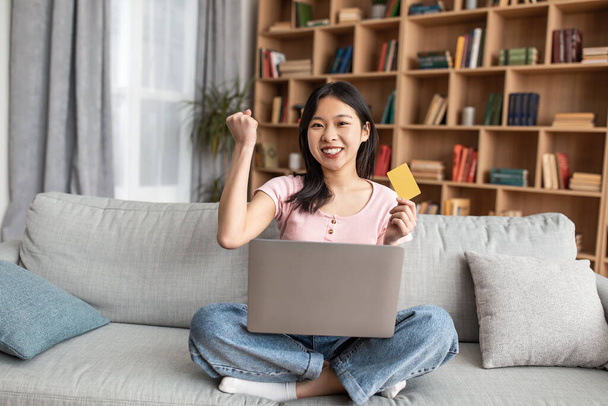 Boldog koreai nő laptoppal és hitelkártyával, hogy IGEN gesztus nagy kedvezmény, otthon ül - Fotó, kép
