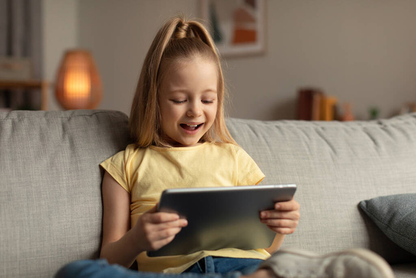 Cheerful Little Girl Using Digital Tablet Browsing Internet At Home - Foto, immagini