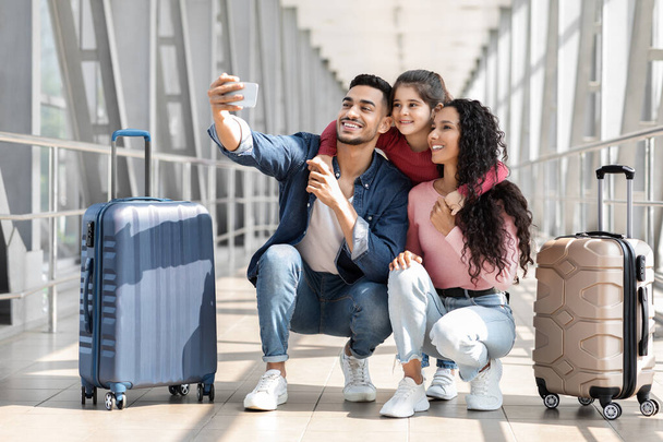 Alegre familia de Oriente Medio de tres tomar selfie con Smartphone en el aeropuerto - Foto, imagen