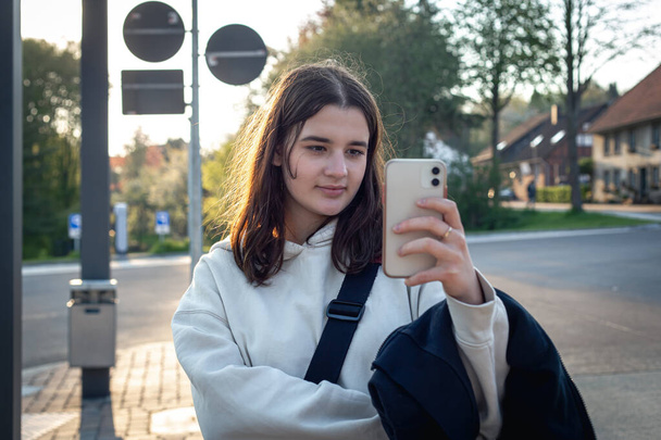 Eine junge Teenagerin wartet frühmorgens an einer Bushaltestelle auf einen Bus. - Foto, Bild