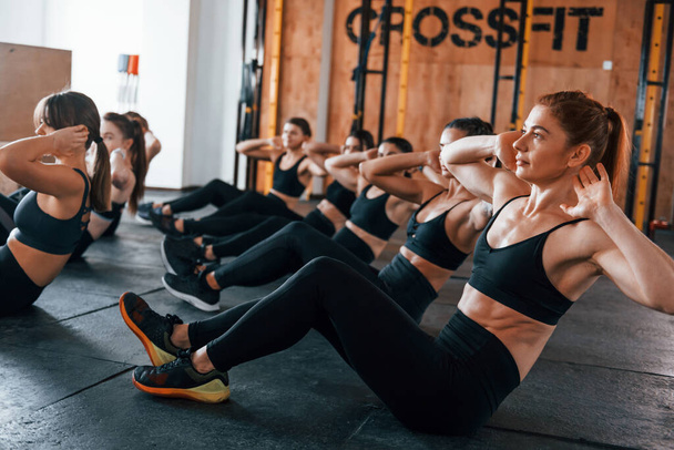 Doing abs. Group of young sportive people have crossfit day indoors in gym. - Fotografie, Obrázek