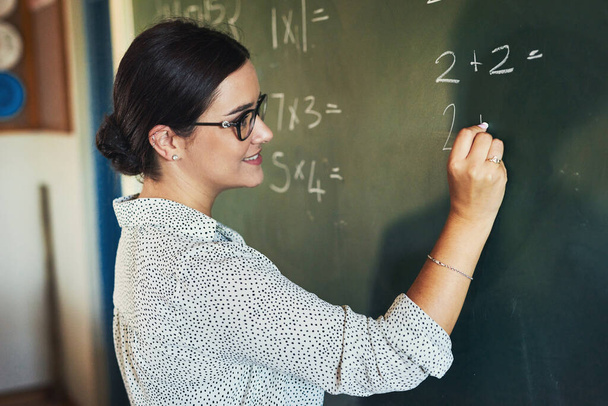 Testing my students on their math skills. Shot of an attractive young teacher standing alone and writing on the blackboard during a lesson in her classroom. - Fotoğraf, Görsel