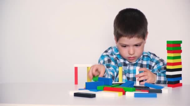 Egy 4 éves fiú többszínű fablokkokkal játszik, tornyokat épít fehér alapon. Természetes játékok a gyermekek logikai és motoros készségeinek fejlesztésére. - Felvétel, videó