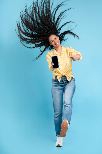 Cheerful lady jumping and pointing at empty smart phone screen - Foto, imagen