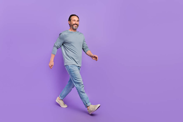 Full size profile portrait of satisfied adult person walking look empty space isolated on purple color background - Foto, Imagem