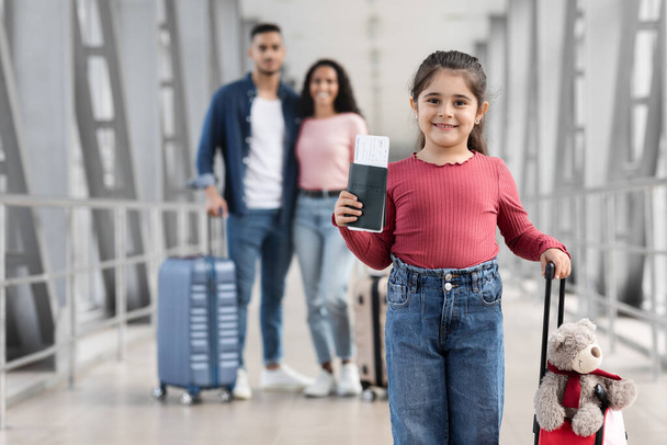 Mała Arabka z walizką i paszportem pozowanie na lotnisku z rodzicami - Zdjęcie, obraz