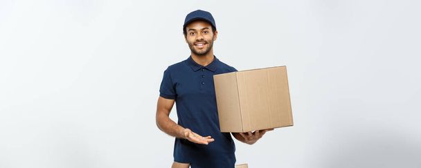 Delivery Concept - Portrait of Happy African American delivery man pointing hand to present a box package. Isolated on Grey studio Background. Copy Space. - Photo, Image