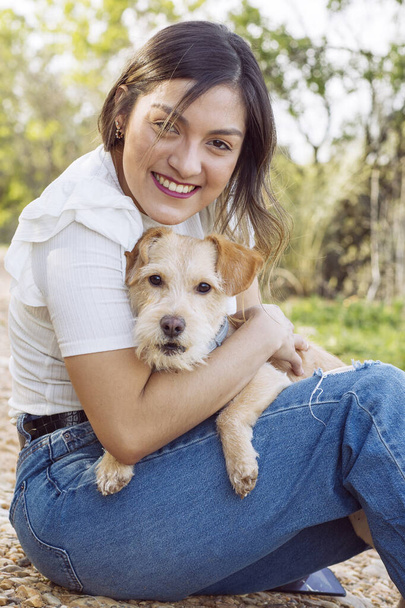 Nuori nainen hymyilee ja halaa koiraansa istuessaan polulla - Valokuva, kuva