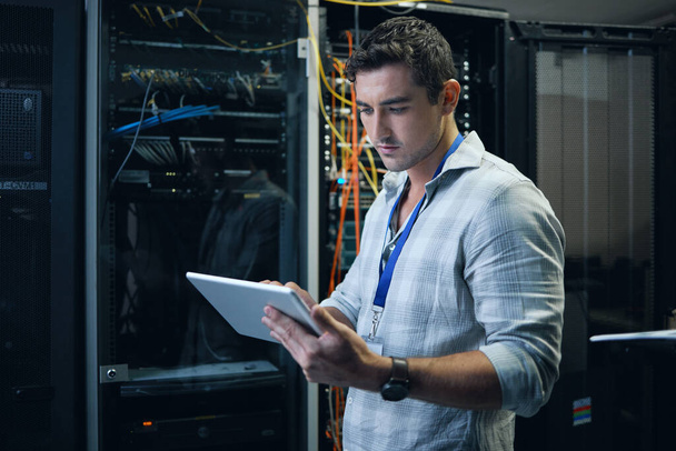 Checking the network status. Cropped shot of a handsome young male programmer working on a tablet in a server room. - Photo, Image